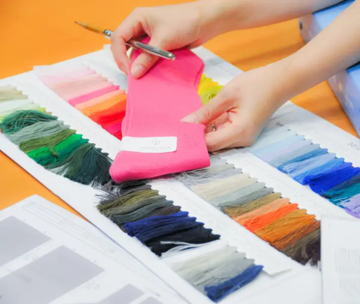 A photo of a person holding and overlapping fabric materials on a colorful thread color swatch to check the color.